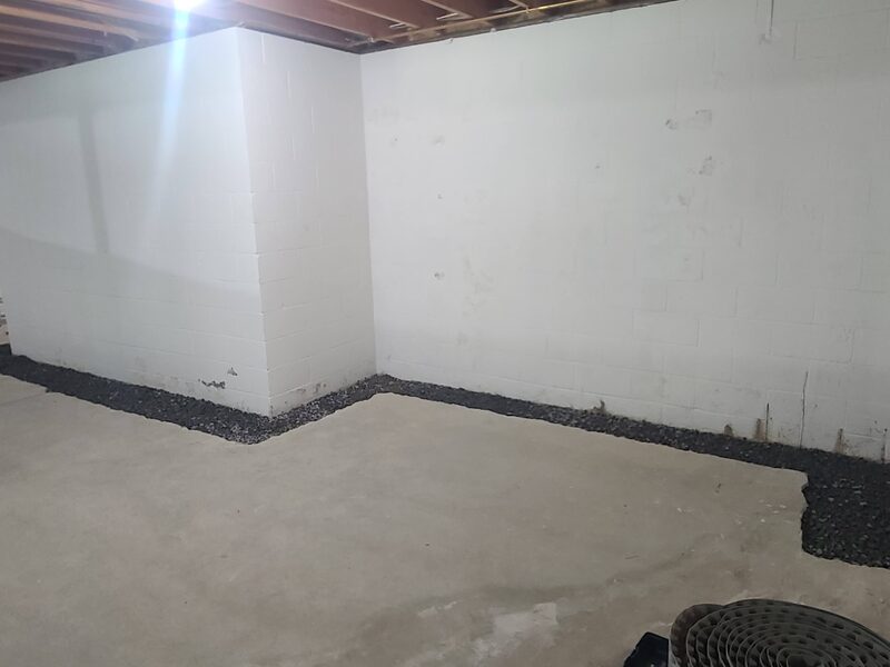 Basement walls covered with white panels down to the floor, with a dimpled drainage edge running along the bottom of the walls before the floor is finished