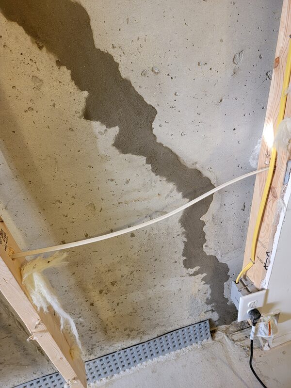 Wet stain spreading down a poured concrete basement wall from a crack, with a new interior drain channel along the floor, in a Quarryville, PA home