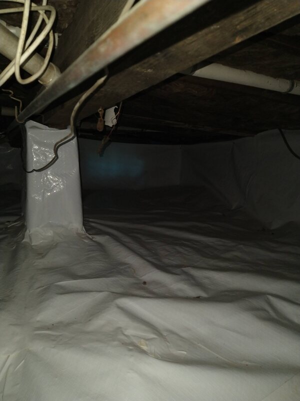 Support pier inside a crawl space wrapped in white vapor barrier, with the liner covering the ground and running up the walls